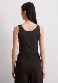 Top aderente verde scuro con design a scollo rotondo, abbinato a pantaloni marroni scuri a vita alta con tasca laterale e texture liscia.
