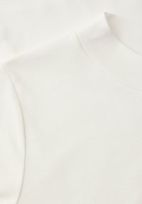 Gros plan sur un tissu blanc montrant un col montant et une texture lisse, mettant en valeur les détails de l'encolure et de la couture d'épaule.