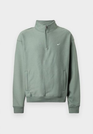 Svetlo zelena Nike pulover s četrtinskim zadrgo, rebrastimi manšetami in stranskimi žepi. Mehka tekstura in minimalno označevanje z majhnim logotipom na prsih.
