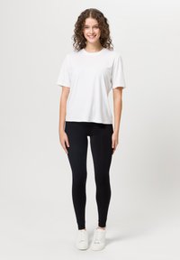 Maglietta bianca a maniche corte abbinata a leggings neri e sneakers bianche. Il tessuto appare liscio; la maglietta ha una vestibilità comoda e un collo rotondo.