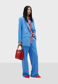 Blue tailored suit with double-breasted blazer, paired with a red patterned blouse and red handbag. Pointed red shoes complete the look.