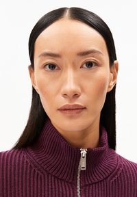 Paarse geribde gebreide trui met een hoge kraag en zilveren rits. De gladde textuur en de gedefinieerde lijnen benadrukken het moderne ontwerp.