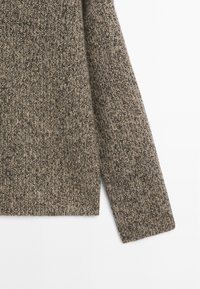 Manica e parte inferiore del torso di un maglione lavorato a maglia marrone e beige mélange con texture a coste su sfondo bianco.