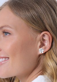 Silver flower-shaped stud earring with five textured petals. Close-up view highlighting the design and attached to a model's ear.