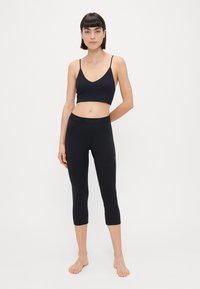 Bralette atlético preto e leggings de três quartos, ambos em um tecido liso e elástico. O bralette apresenta alças finas; a legging tem uma cintura com logotipo.