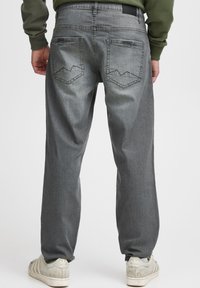 Pelēkas džinsa bikses ar brīvu piegriezumu, ar izšūtām aizmugurējām kabatām kalnu motīvā. Valdātas ar gaiši krāsām sporta apaviem.