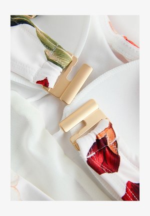 Bílá látka s květinovými akcenty, vybavená zlatými kovovými zapínáními, s hladkou texturou a sbíranou částí na popruhu.