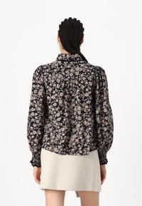 Blusa de estampado floral en azul marino oscuro con flores rosa claro. Cuenta con mangas abullonadas, cuello con solapa y puños fruncidos, hecha de tejido ligero.
