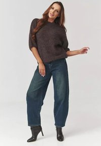 Luźny, teksturowany sweter w ciemnym brązowym kolorze z krótkimi rękawami, zestawiony z niebieskimi jeansami o wysokim stanie i czarnymi botkami za kostkę.