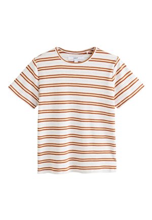 Kvinde med langt krøllet hår bærer en hvid t-shirt med brune vandrette striber og en blå denimnederdel, vendt væk fra kameraet.