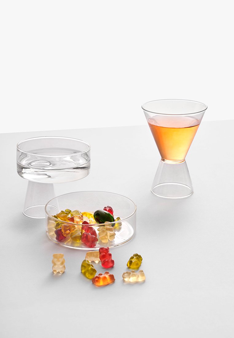 Przezroczysty zestaw szkła zawiera okrągłe naczynie z żelkami, cylindryczny kubek oraz stożkowaty kieliszek wypełniony bursztynowym płynem.