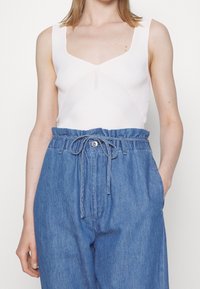 Top bianco a costine senza maniche con scollatura a V, abbinato a pantaloni in denim azzurri chiari a vita alta con coulisse e tasche laterali.