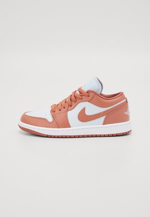 Zapatilla deportiva baja en blanco y naranja suave, con el logo Nike Swoosh, puntera perforada y una suela blanca con banda de rodadura naranja.