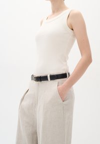 Beige ribbad linne topp i kombination med ljusbeige linbyxor, med ett svart läderbälte med en guldbuckle.