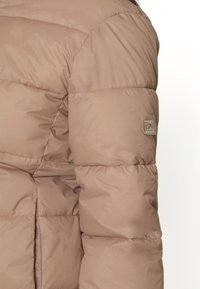 Giacca puffer beige con un design trapuntato, caratterizzata da pannelli cuciti e una patch con logo sulla manica. Tessuto liscio e lucido.