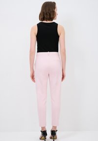 Roze tailored trousers met een gladde textuur, een aansluitende silhoët en een enkele achterzak. Gecombineerd met een zwart mouwloos topje en zwarte hakken.