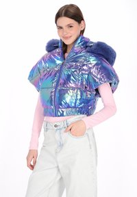 Iryzująca krótka kurtka puchowa z wysokim kołnierzem, zamkiem błyskawicznym i niebieskim sztucznym futerkiem, zestawiona z jasnymi jeansami.