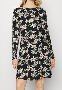 Svart klänning i mjukt tyg med långa ärmar, rund halsringning och ett blommönster av rosa och gröna blommor.