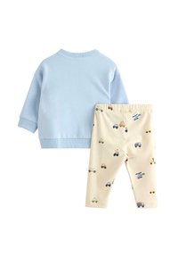 Jasnoniebieska bluza z długimi rękawami i ściągaczami, w połączeniu z kremowymi spodniami z kolorowym wzorem samochodów i pojazdów.