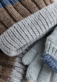 Stickade handskar och halsduk i gråa och bruna nyanser. Har ribbade och tvistade mönster med varierande texturer och kontrasterande färger.