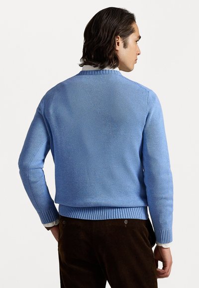 Pull en tricot bleu clair avec un ourlet et des poignets côtelés, associé à un pantalon en velours côtelé marron foncé, vu de dos.