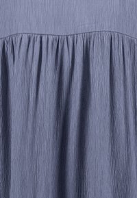 Crinkled fabric dress in a muted blue shade. Features a gathered waistline with subtle texture and softness throughout the fabric.