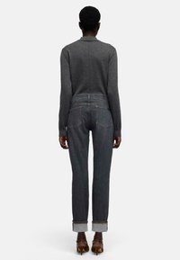 Szary top z długim rękawem w połączeniu z ciemnymi dżinsami z podwiniętymi mankietami i dopasowanym krojem. Widok z tyłu podkreśla czyste linie i minimalistyczne detale.