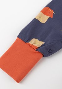 Long-sleeve garment featuring a navy blue body with a soft orange cuff. Patterned with light-colored shapes and outlines. Buttons at the cuff.