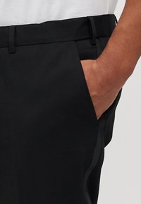 Black trousers with side pockets, made from smooth fabric. Features a flat front with a subtle sheen and belt loops.