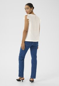 Top blanc à manches évasées associé à un jean droit bleu et des chaussures noires à petits talons. Tissu lisse, design simple et tons neutres.