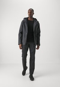 Black waterproof jacket with a hood, featuring a textured fabric. Paired with dark, fitted pants and black shoes.
