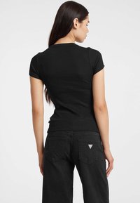 T-shirt nera a costine con maniche corte, scollatura rotonda e design aderente. Abbinata a pantaloni neri con tasche posteriori e dettaglio del logo.