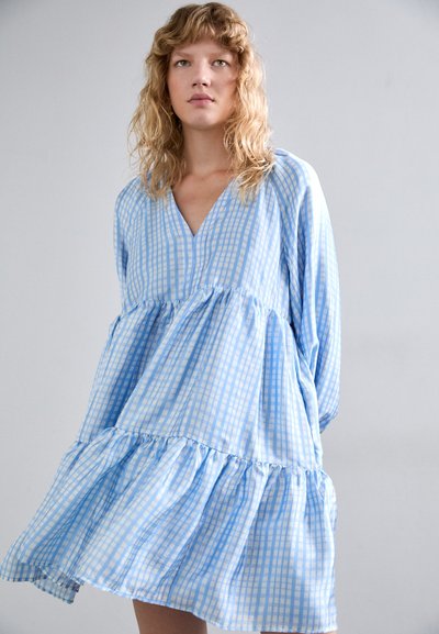 Robe à carreaux vichy bleus et blancs avec un col en V, des manches longues et un ourlet à volants. Fabriquée en tissu léger avec une coupe décontractée.