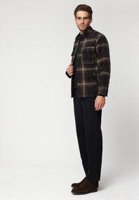 Koszula w kratę w ciemnych odcieniach z wzorem w kratę, z przednią kieszenią i zapięciem na guziki. Ciemne spodnie i brązowe botki za kostkę.