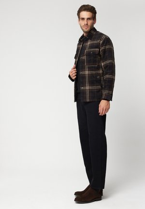 Koszula w kratę w ciemnych odcieniach z wzorem w kratę, z przednią kieszenią i zapięciem na guziki. Ciemne spodnie i brązowe botki za kostkę.