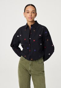 Zwarte overhemdbloes met kleurrijke hartborduursels. Beschikt over een klassieke kraag en lange mouwen, gemaakt van gladde stof voor een ontspannen pasvorm.