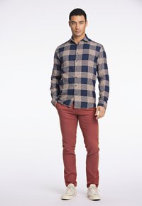 Camisa de hombre de botones con un patrón a cuadros en navy y beige, de mangas largas, combinada con pantalones rojos y zapatillas blancas.