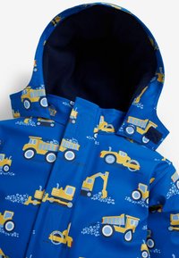 Geacă de ploaie albastră cu un imprimeu de vehicul de construcție galben, material impermeabil și căptușeală moale din fleece bleumarin în interiorul glugii.