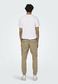 Pantalons cargo beige avec poches latérales, poignets élastiques et coupe décontractée, assortis à un t-shirt blanc à manches courtes et des baskets blanches.
