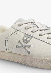 Sneaker in suede bianco con design grigio di teschio e incrocio di ossa, suola testurizzata e dettagli perforati lungo il lato. Presenta lacci grigi coordinati.