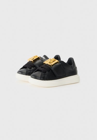 Svarta lädersneakers med en texturerad yta, med accent av ett guldspänne, svarta snören och en vit gummisula.