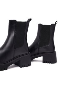 Bottes noires en cuir avec des panneaux élastiques sur les côtés, talons épais et semelles rainurées. Présente une texture lisse et un design simple.
