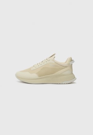 Light beige athletic shoes with a textured upper, mesh panels, and a thick, ridged sole. Features subtle branding on the side.