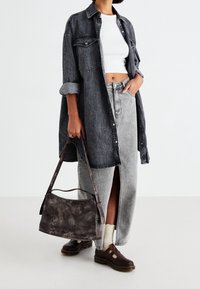Donna che indossa un giubbotto di denim oversize scuro, top corto bianco, gonna midi grigia con spacco, scarpe scure, calzini bianchi e porta una borsa in pelle scura.
