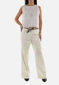 Top bianco senza maniche con motivo in pizzo e orlo a scallop abbinato a pantaloni larghi a vita alta color crema, accentuati da una cintura stampata.