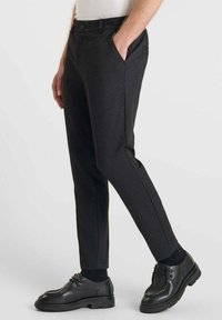 Zwarte op maat gemaakte broek van gestructureerde stof, met een slim fit, zijzakken en een klassieke tailleband, gecombineerd met zwarte schoenen.
