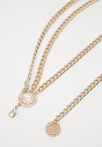 Collana a catena a strati in tono oro con maglie testurizzate, pendenti a medaglione decorativi e chiusura. Presenta dettagli intricati sui pendenti.