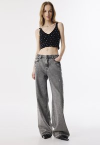 Top corto negro sin mangas con lunares blancos y dobladillo en forma de ondas; jeans gris de pierna ancha con detalles desgastados y cintura alta.