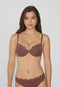 Sostenedor marrón con encaje en los bordes y tirantes ajustables, que presenta copas moldeadas y un borde ondulado. El material suave complementa el diseño.