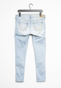 Vaqueros ajustados de color azul claro, confeccionados en denim. Presentan dos bolsillos traseros con costuras contrastantes y una etiqueta en la cinturilla. Cuelga de un gancho negro.